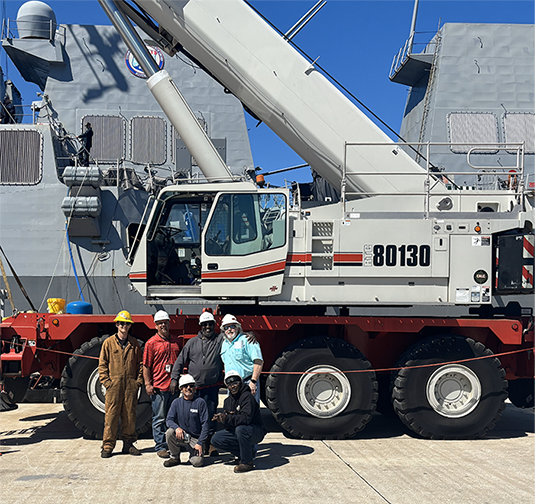 Shipyard workers next to a large crane.
